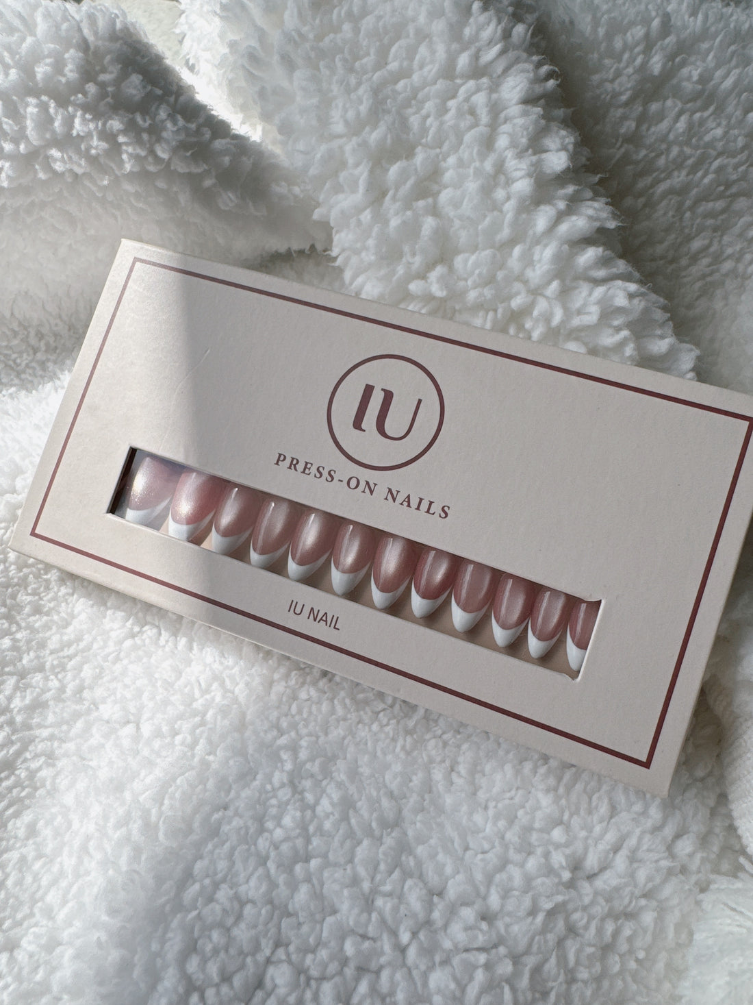 Pink and white French tip press-on nails set in box on soft white fabric background
