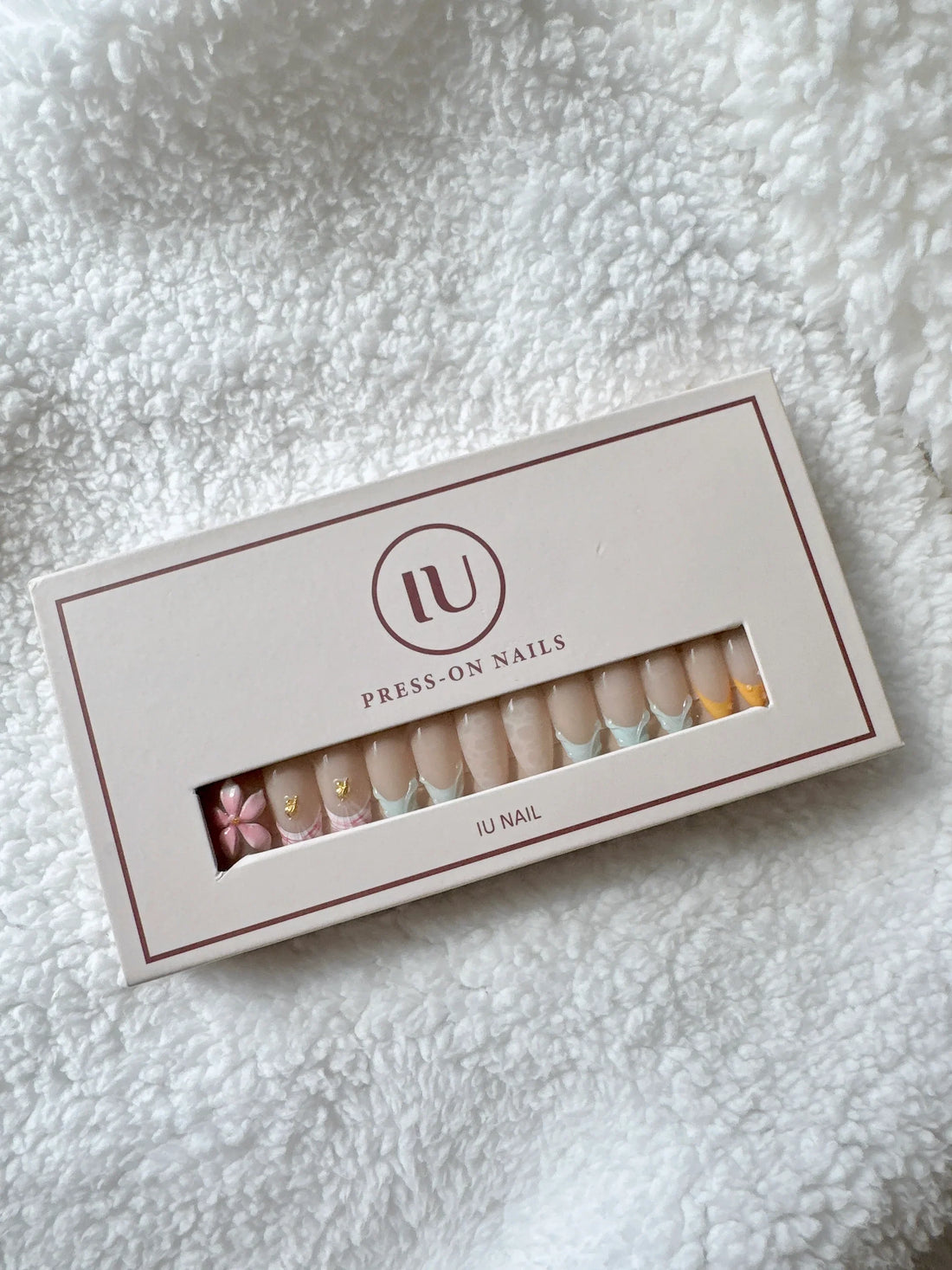 Box of press-on nails with floral and pastel designs on white textured fabric