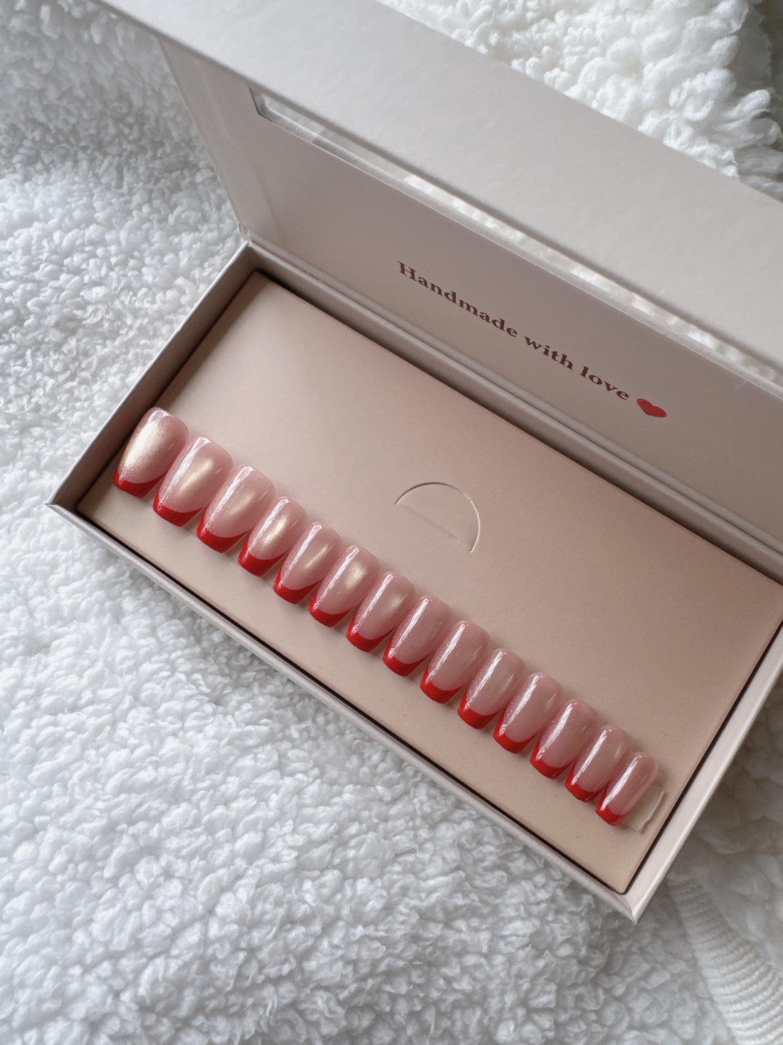 Box of nude pink press-on nails on white textured fabric background