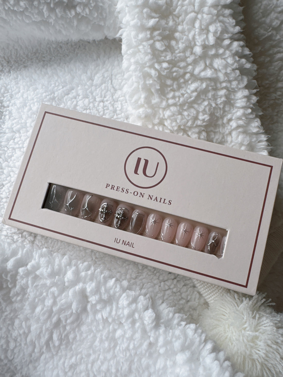 Box of nude and silver press-on nails with star and jewel accents on a white textured blanket