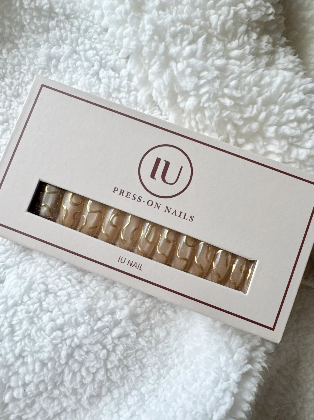 Box of nude and gold press-on nails on white textured fabric background
