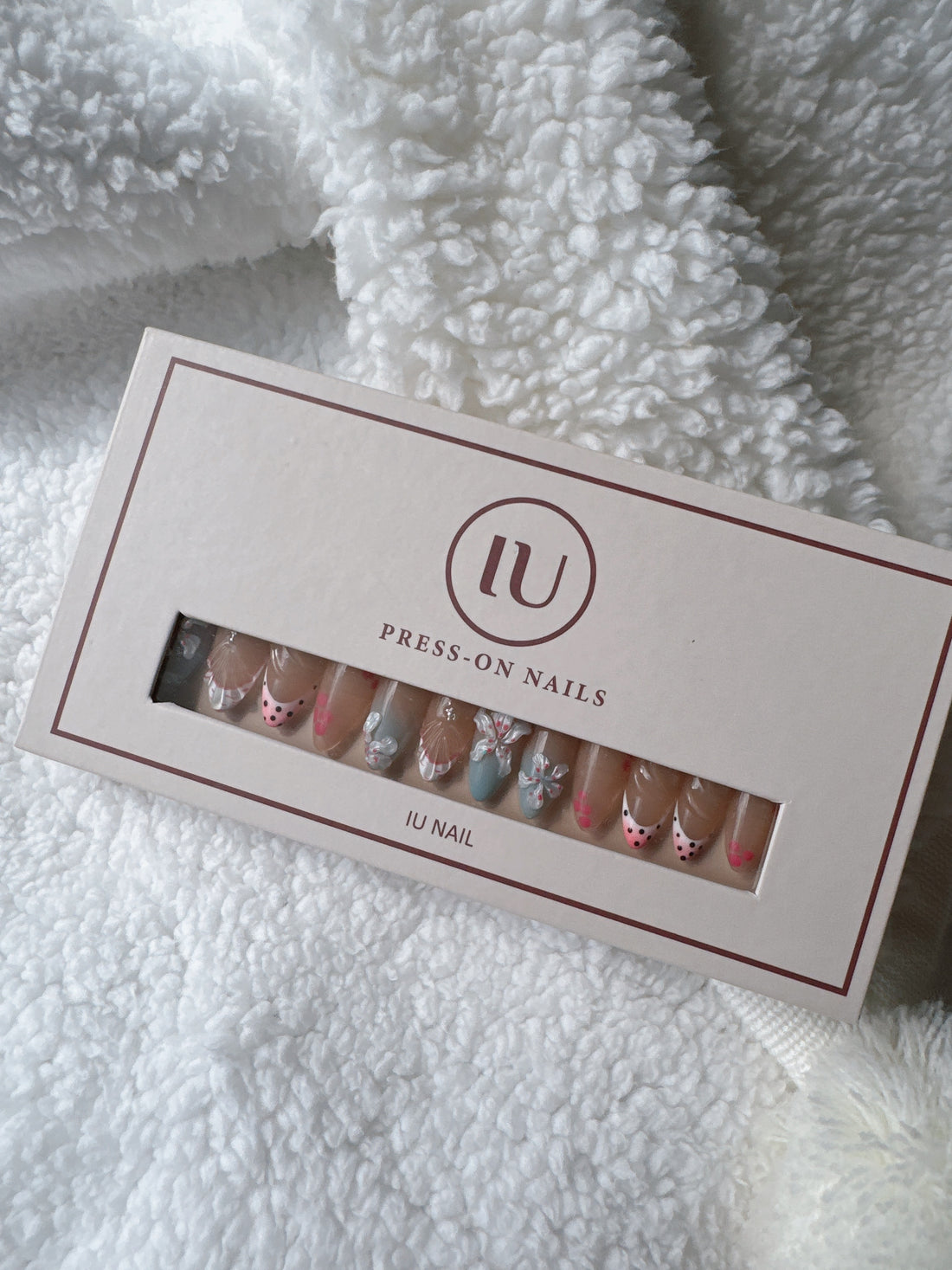 Box of colorful press-on nails with floral and polka dot designs on a white textured blanket.