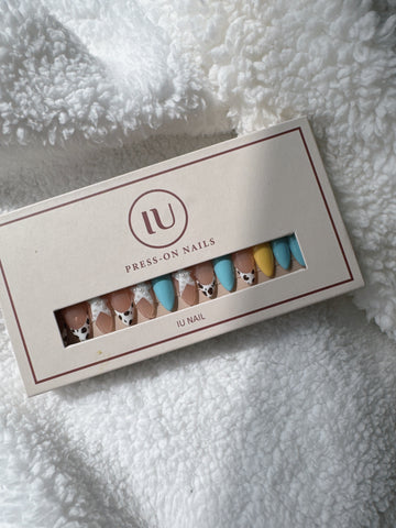 Box of multicolor press-on nails with cow print and pearl accents on white fabric
