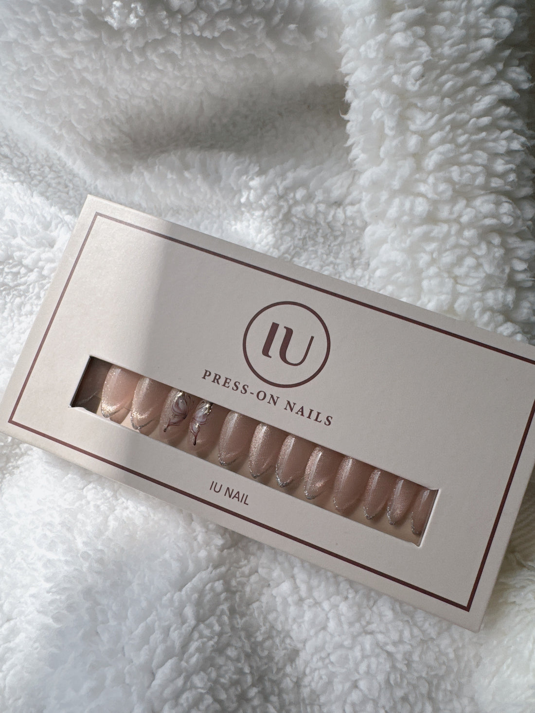 Box of nude press-on nails with silver tips and floral accents on white textured fabric