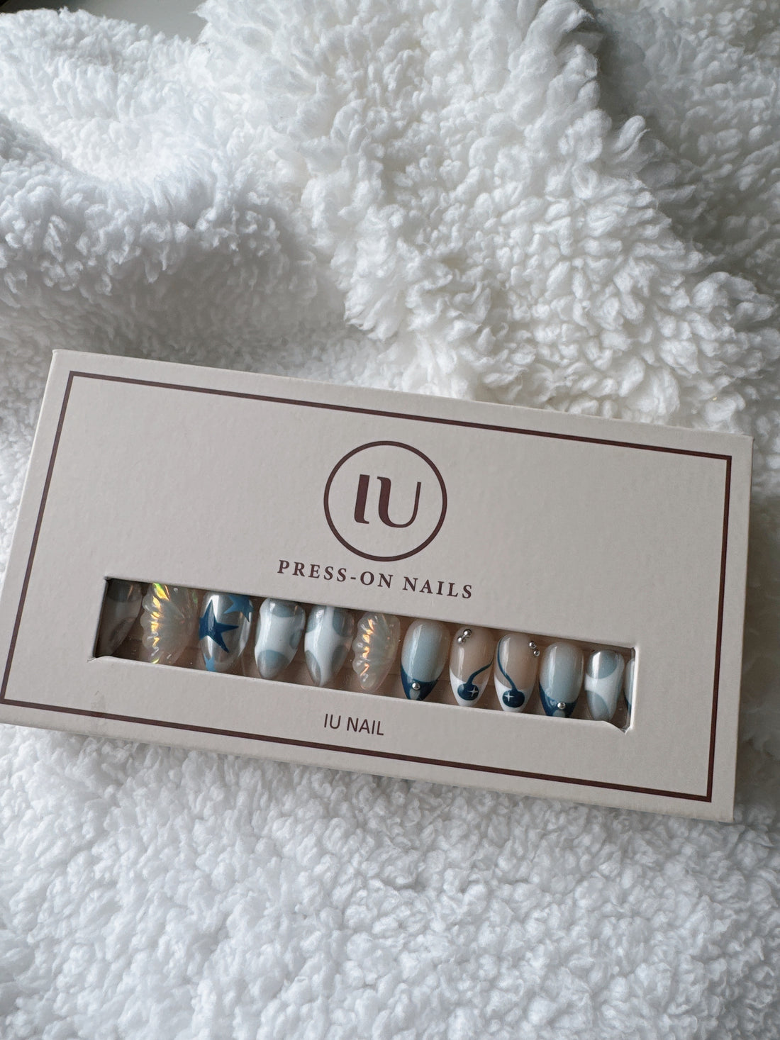Box of press-on nails with blue and white abstract designs on a white textured fabric background