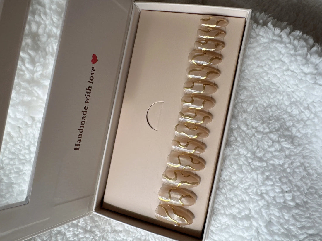 Box of nude and gold press-on nails on white textured fabric background