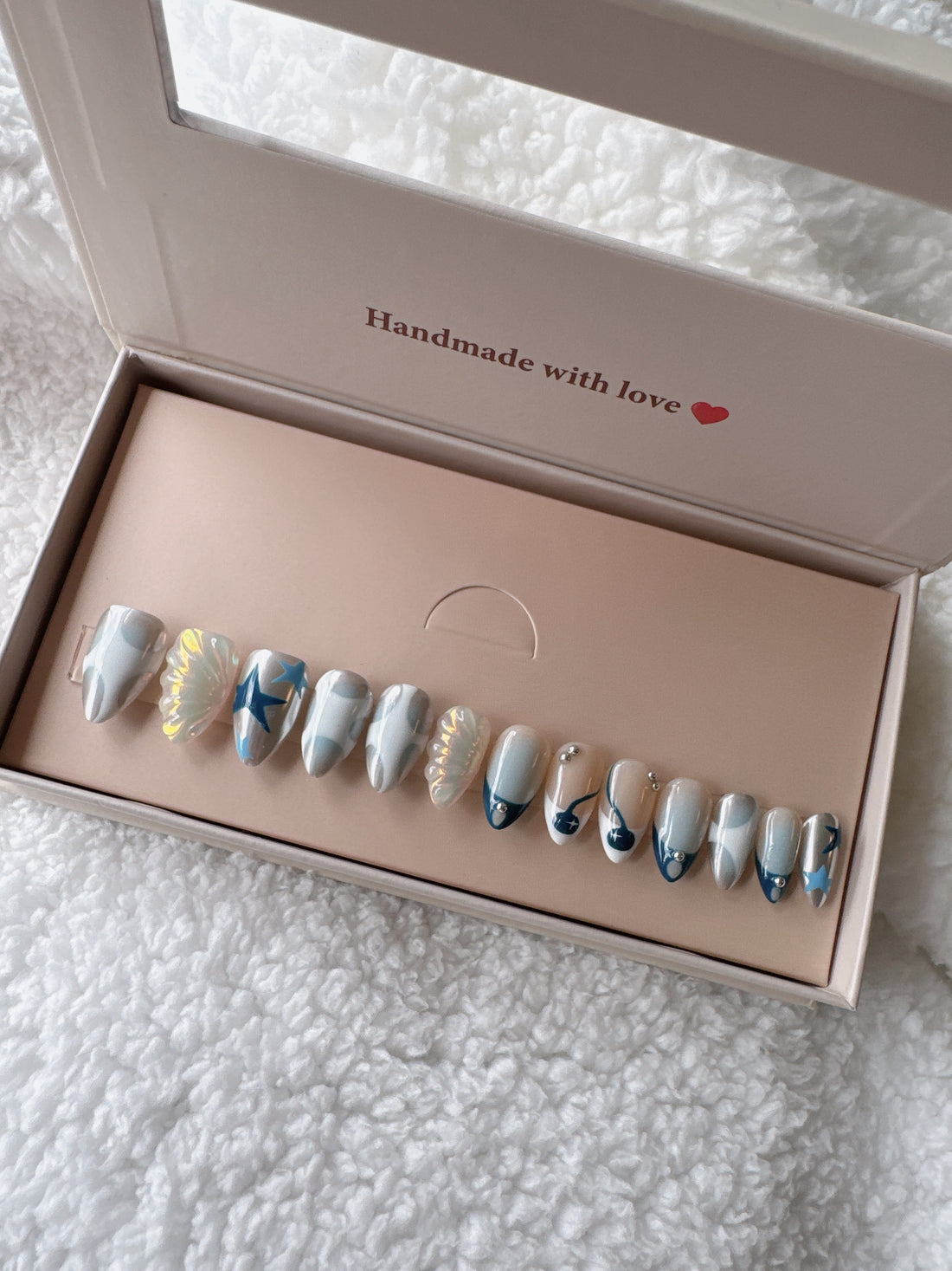 Box of press-on nails with blue and white abstract designs on a white textured fabric background