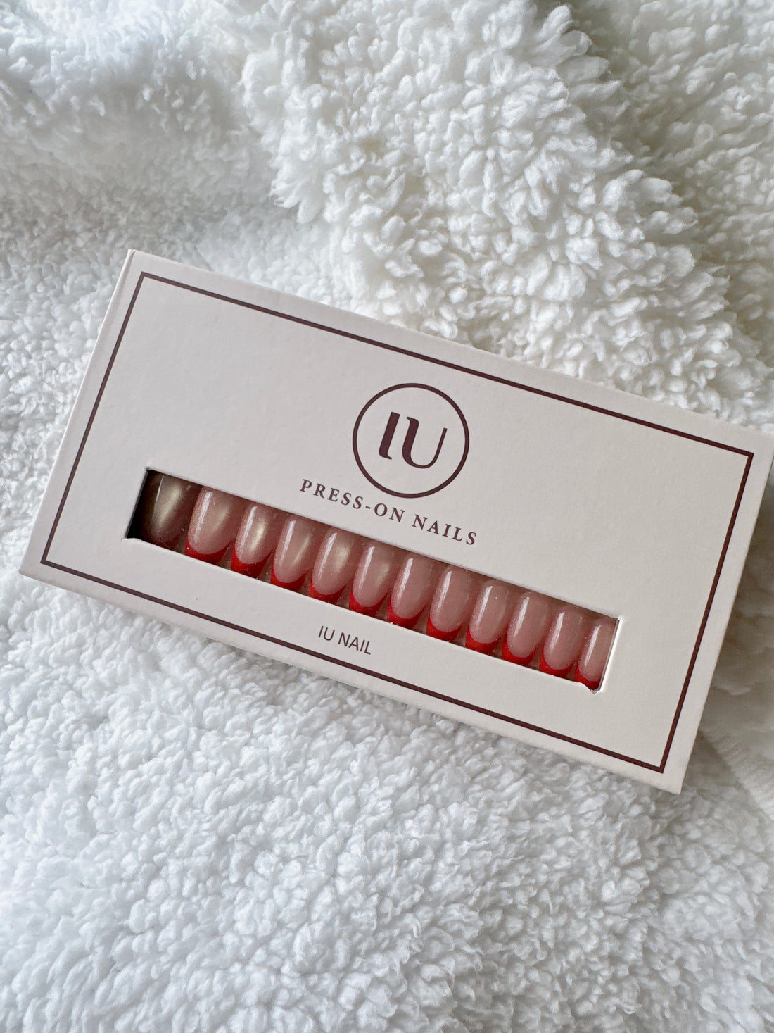 Box of nude pink press-on nails on white textured fabric background