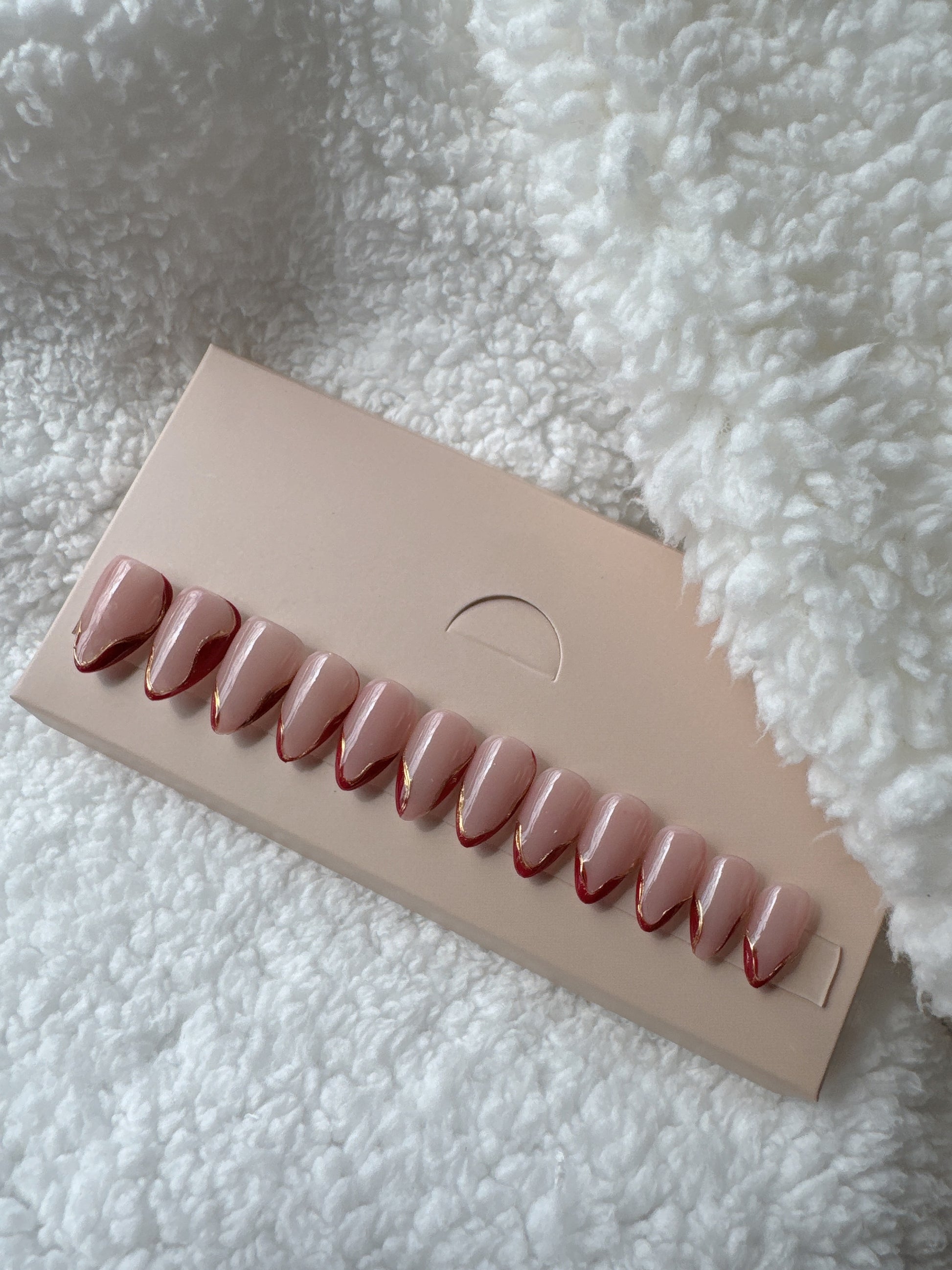 Almond shaped nude press on nails with red and gold French tips on beige card