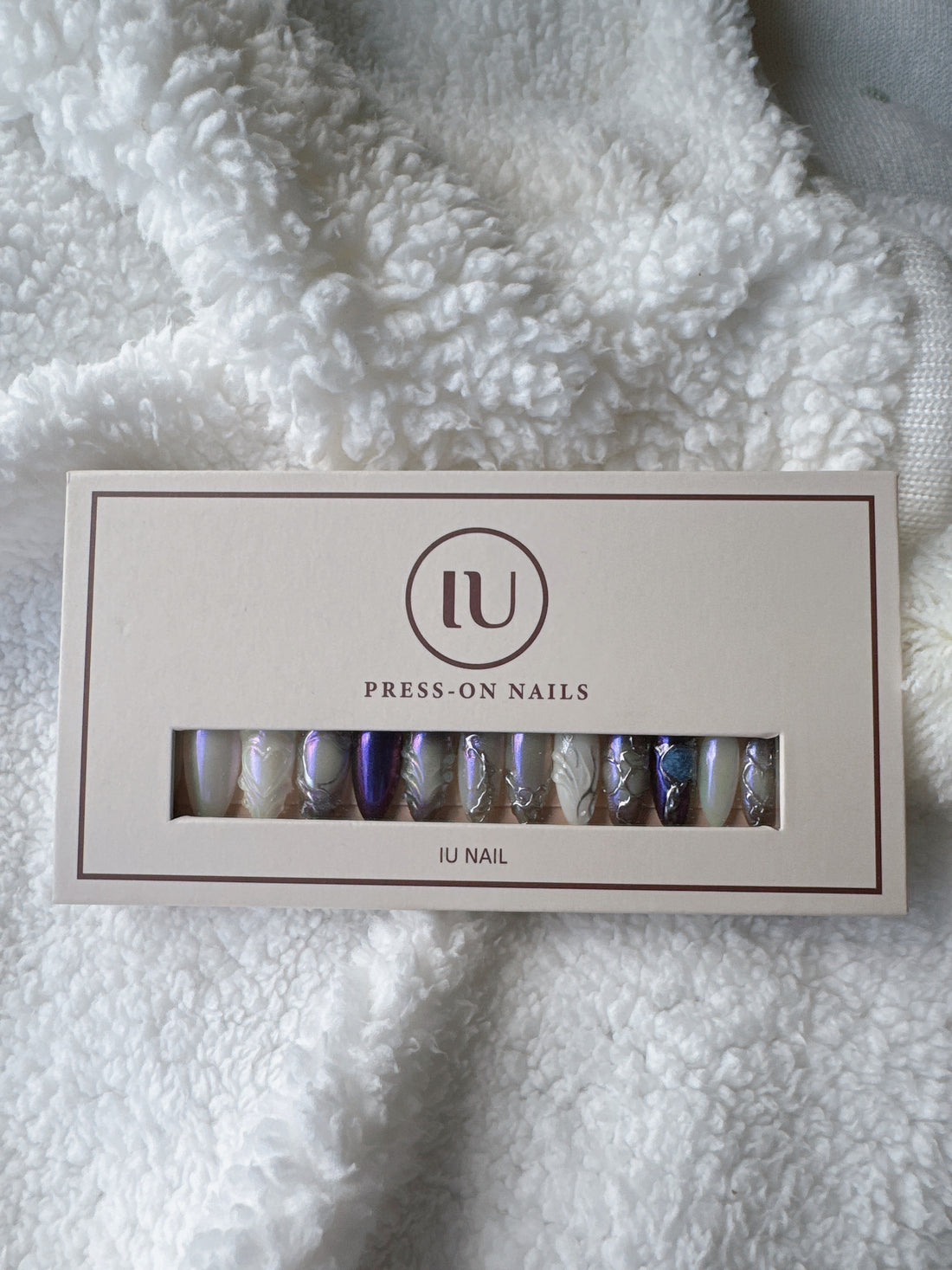 Iridescent press-on nails in a box on white textured fabric background