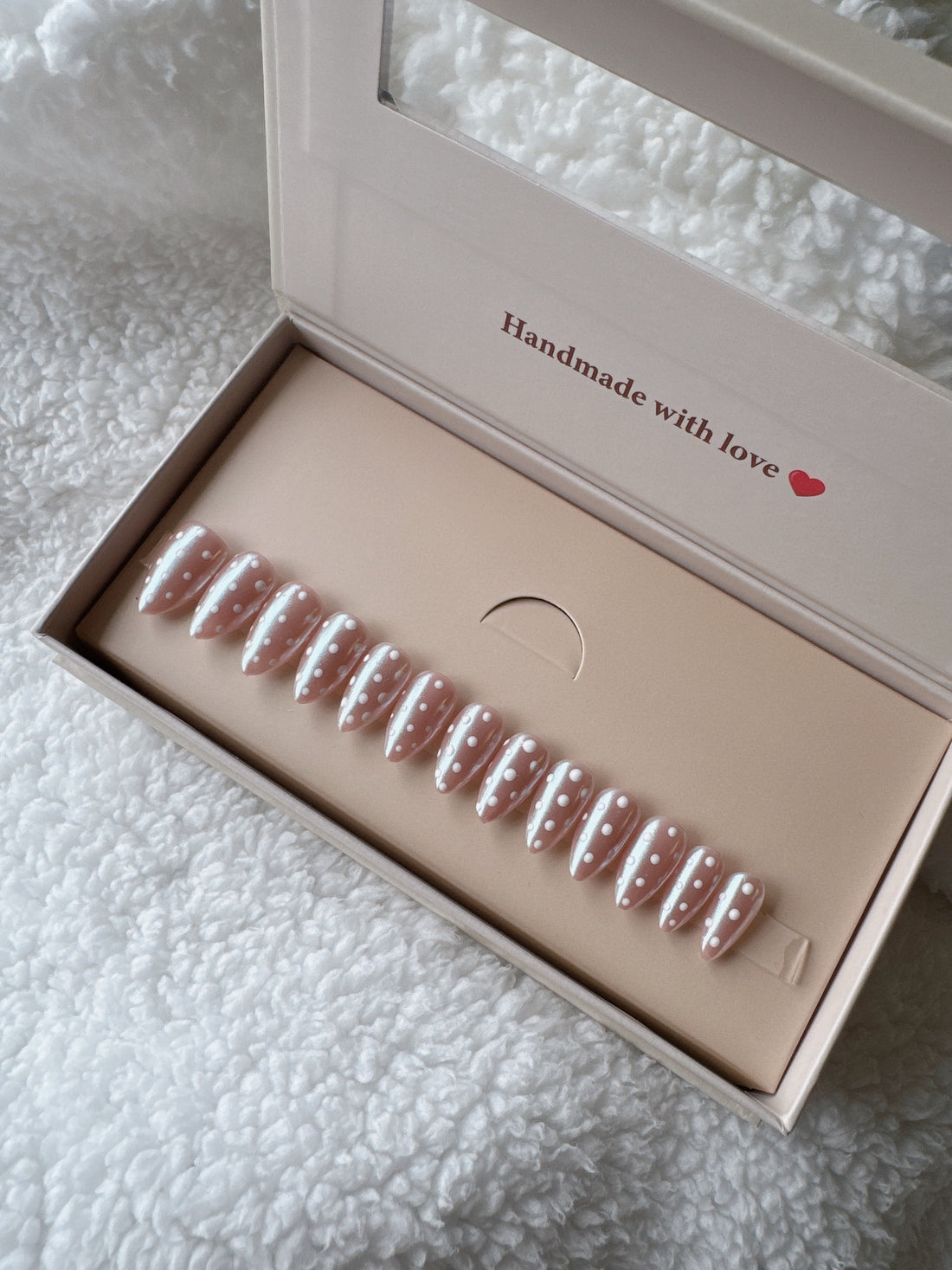 Pink press-on nails with white polka dots in packaging on a soft white textured surface.
