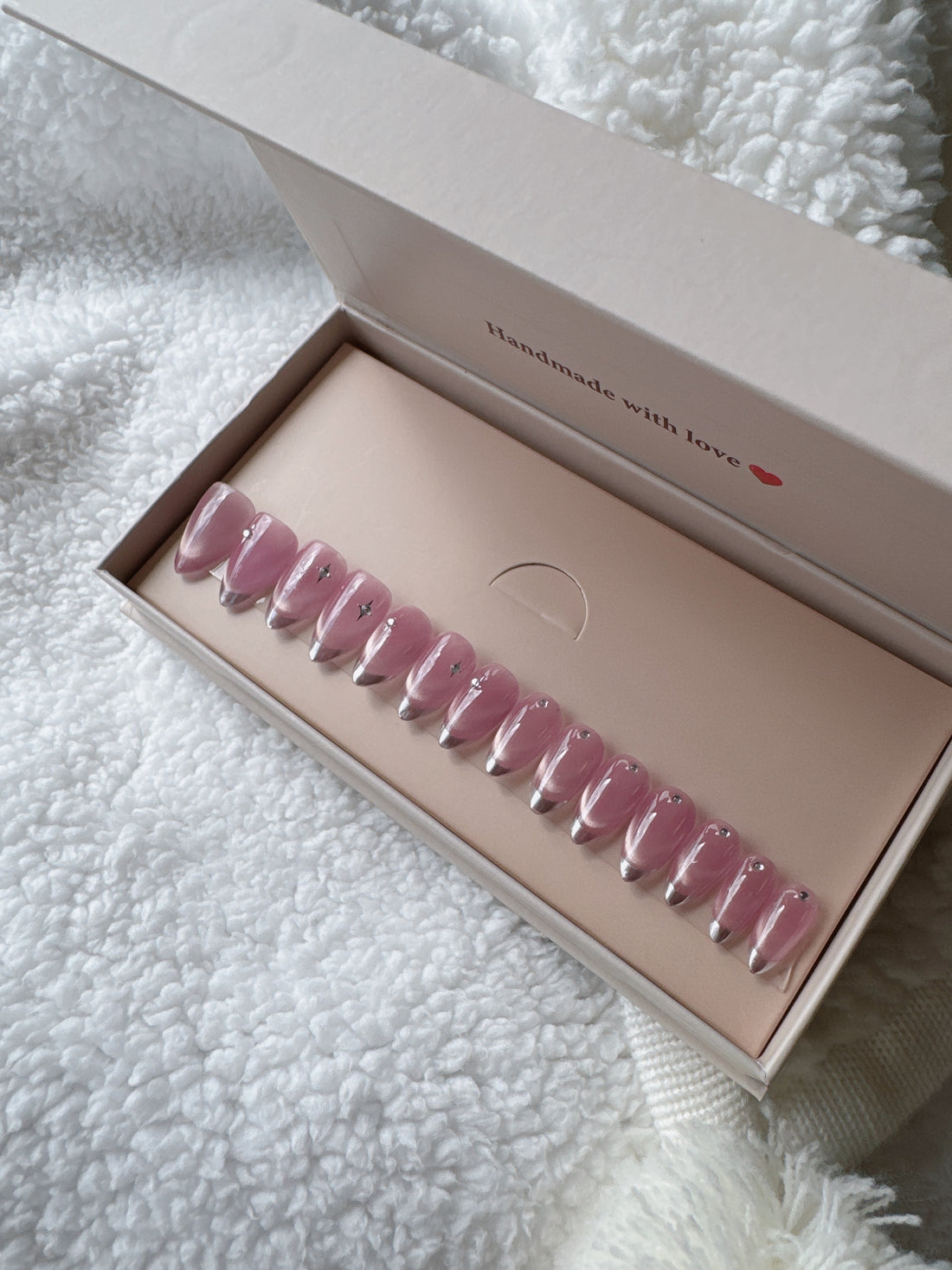 Box of pink press-on nails with small star accents on white textured fabric