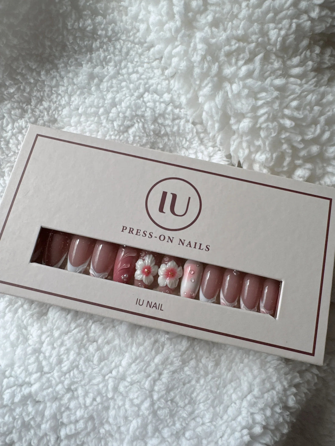 Pink floral press-on nails set in box on soft white textured fabric