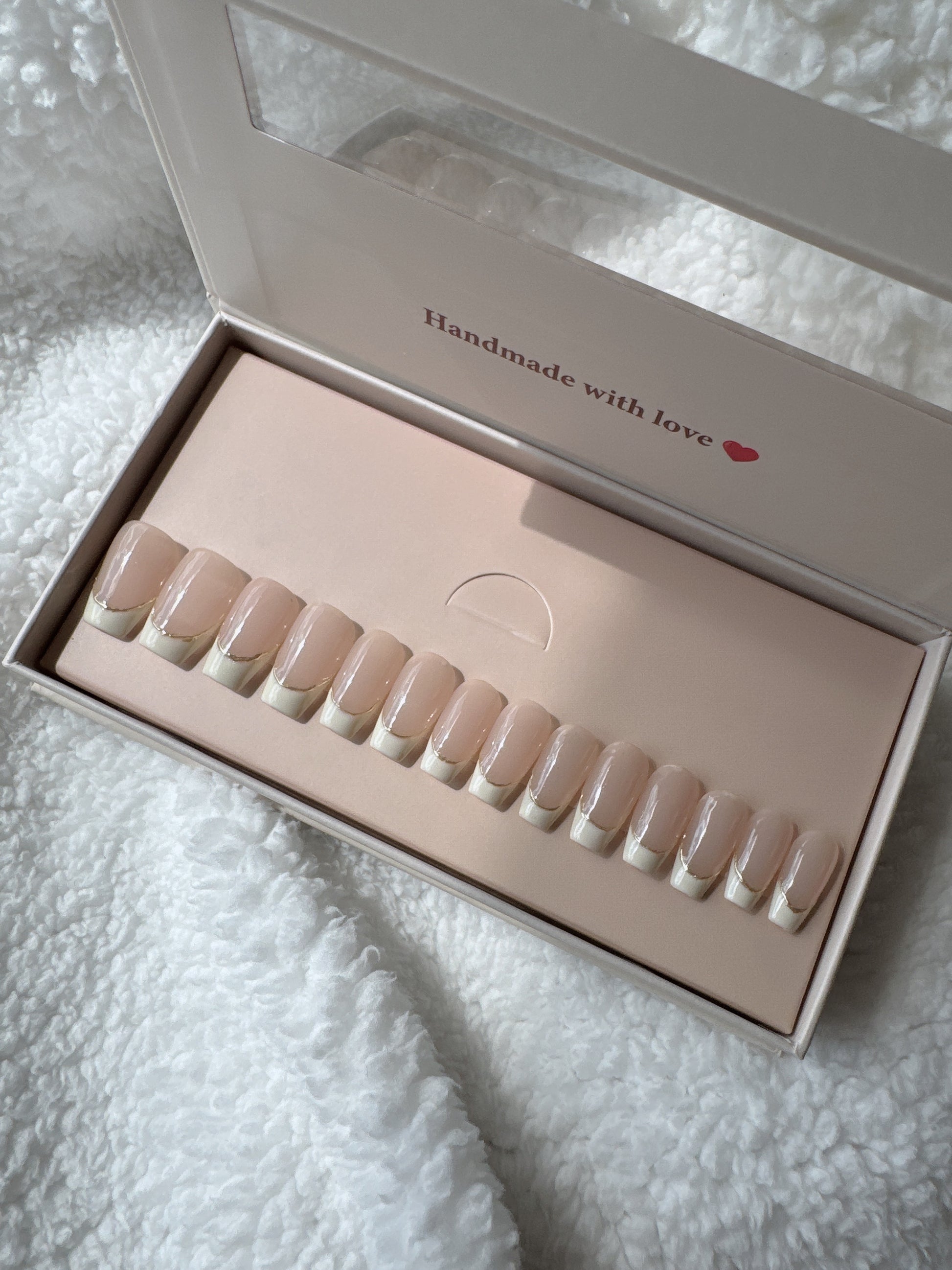Box of handmade nude French tip press-on nails on white textured fabric