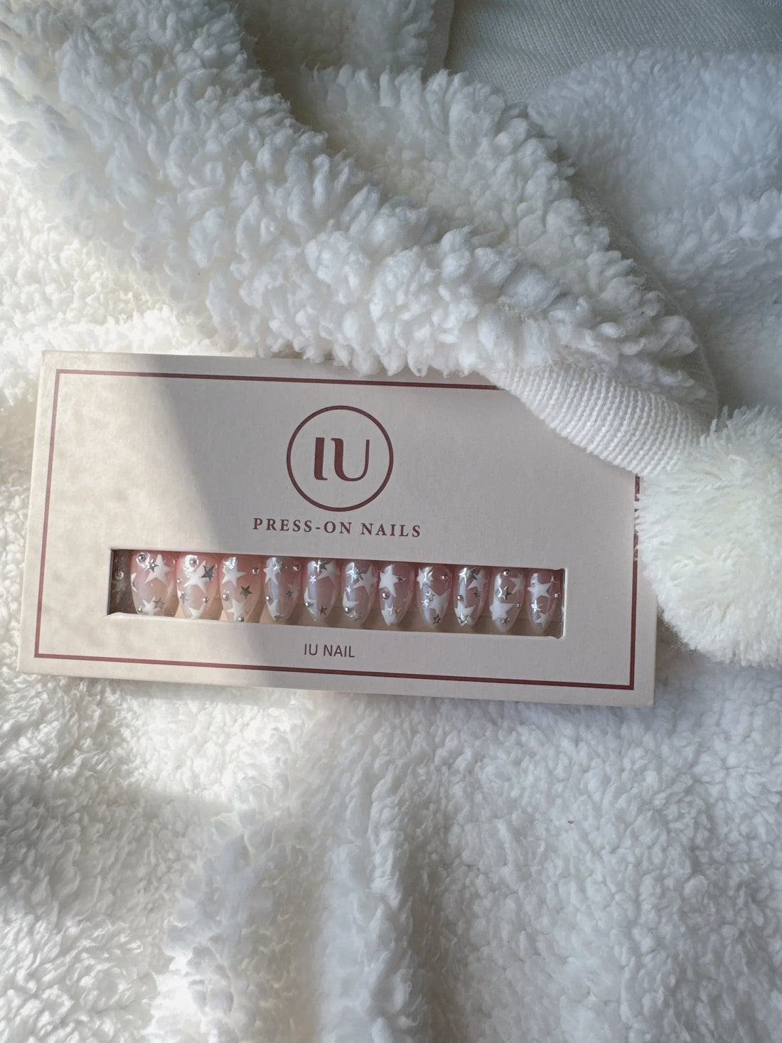 Box of pink press-on nails with white star and rhinestone designs on a soft white blanket