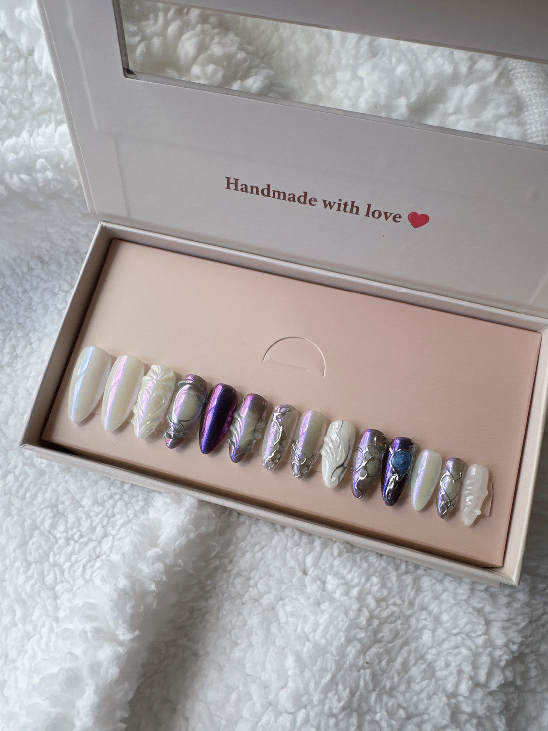 Iridescent press-on nails in a box on white textured fabric background
