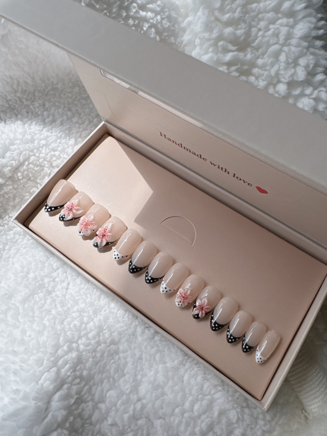 Box of nude press-on nails with black and white polka dot tips and pink 3D floral accents