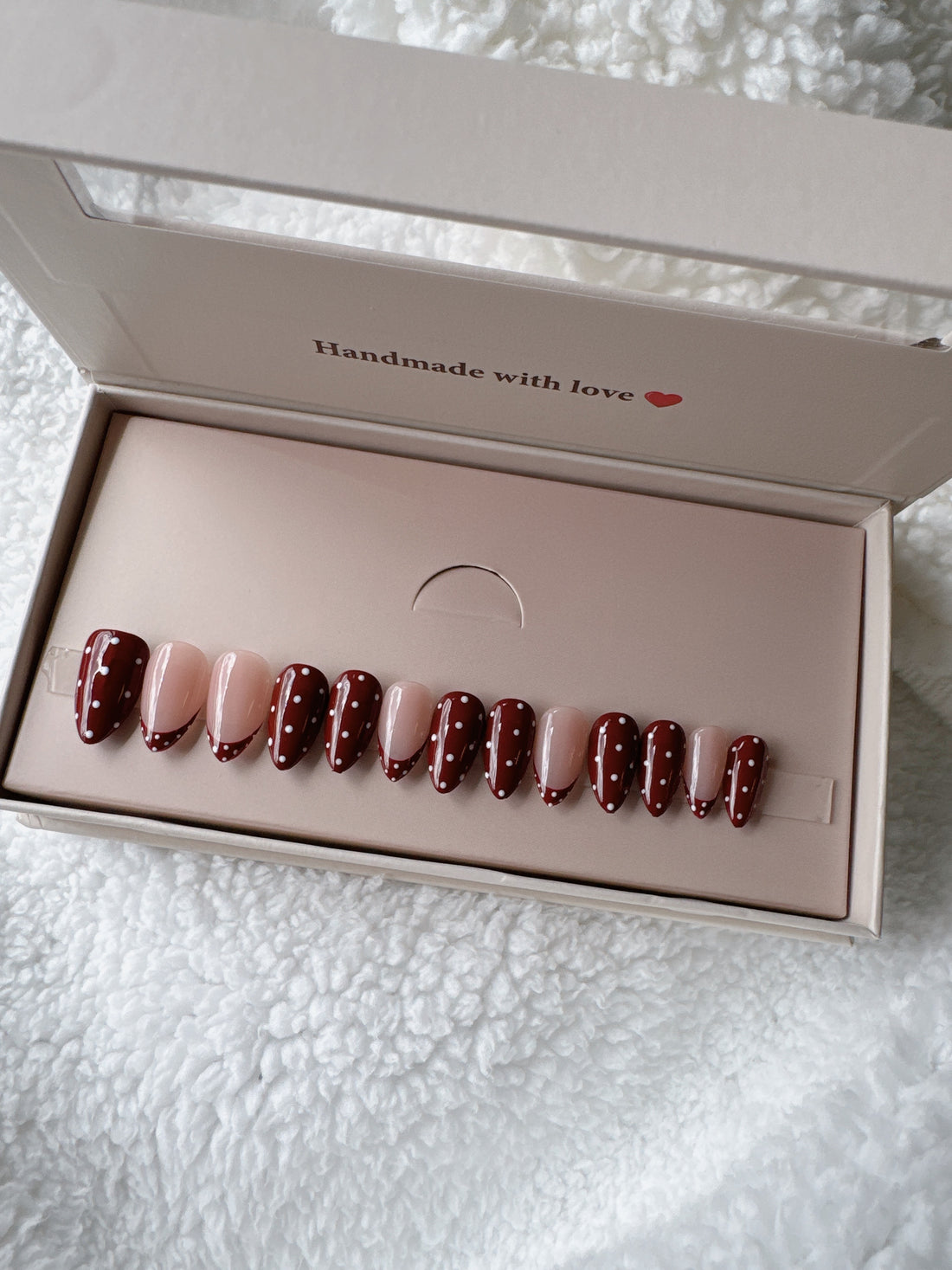 Press-on nails set with red and nude tones, polka dot design in a box on soft white fabric
