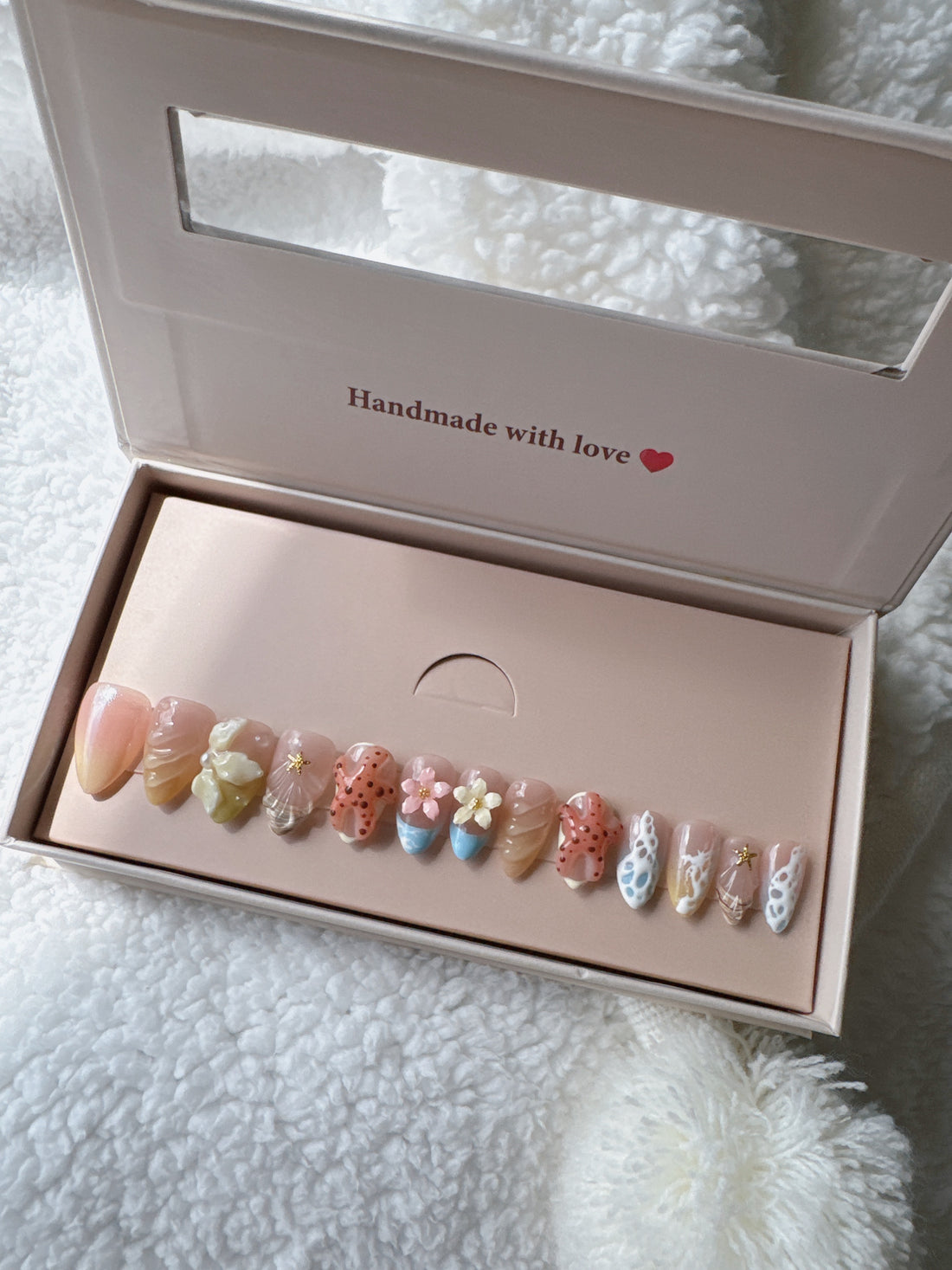 Box of colorful floral press-on nails with 3D designs on white textured fabric