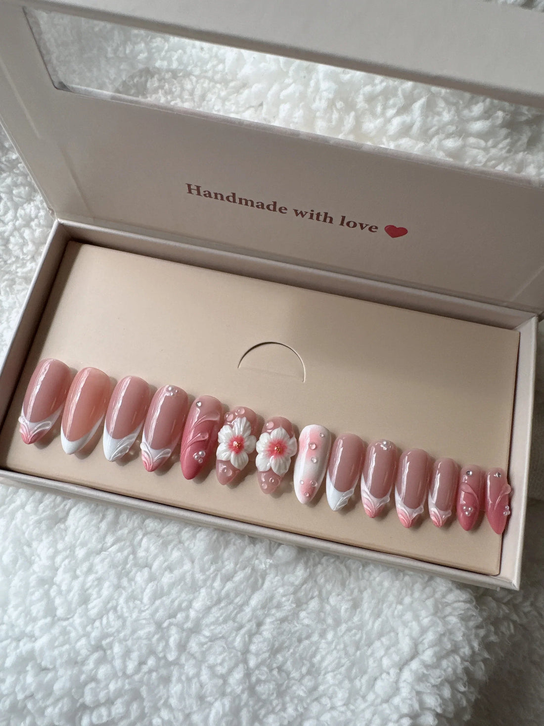 Pink floral press-on nails set in box on soft white textured fabric