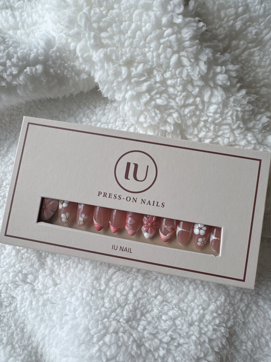 Box of pink floral press-on nails with gold accents on white textured fabric background