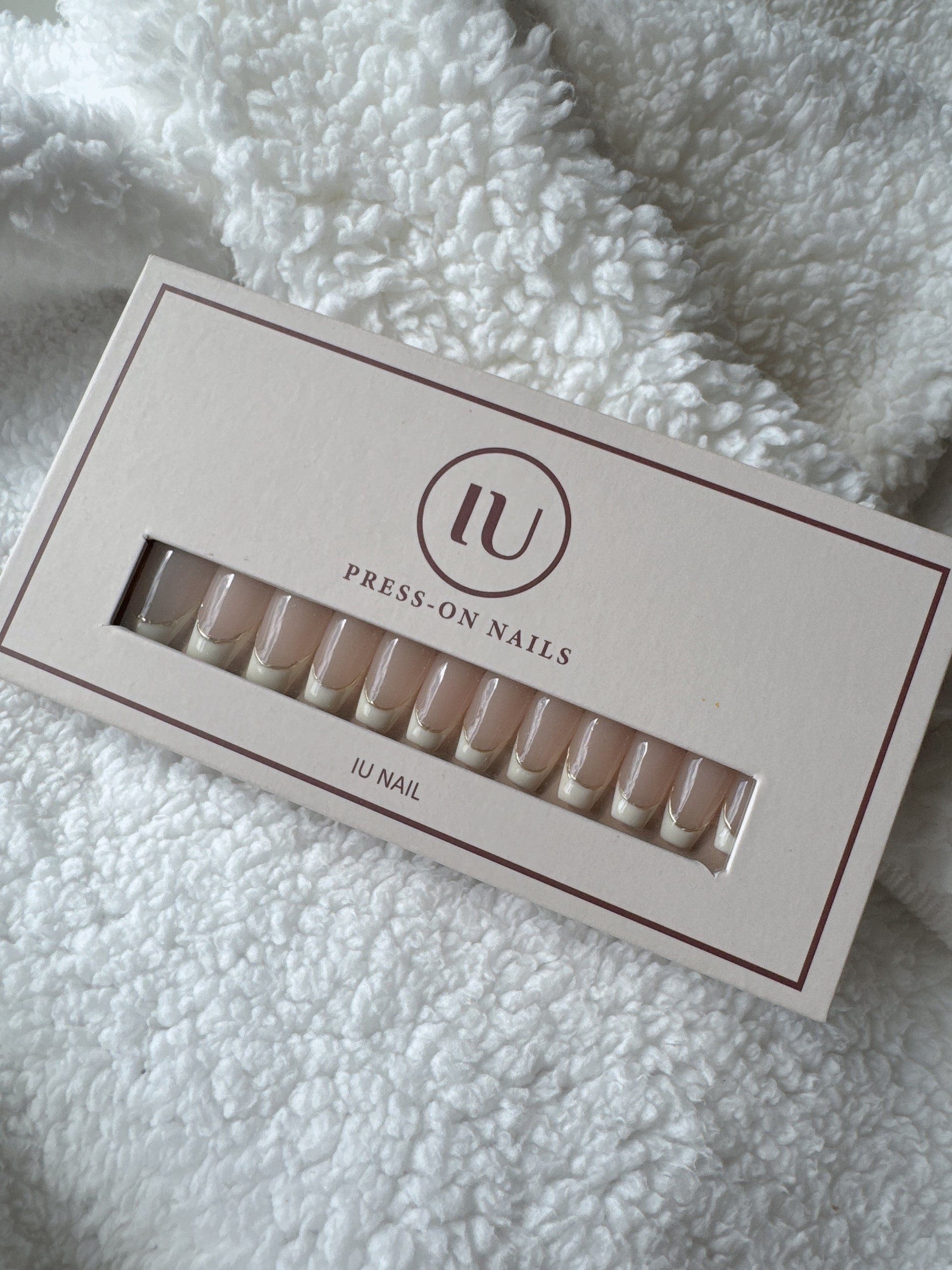 Box of nude French tip press-on nails on a soft white textured fabric background