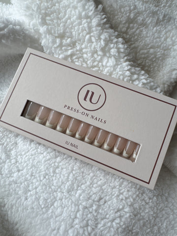 Box of nude French tip press-on nails on a soft white textured fabric background