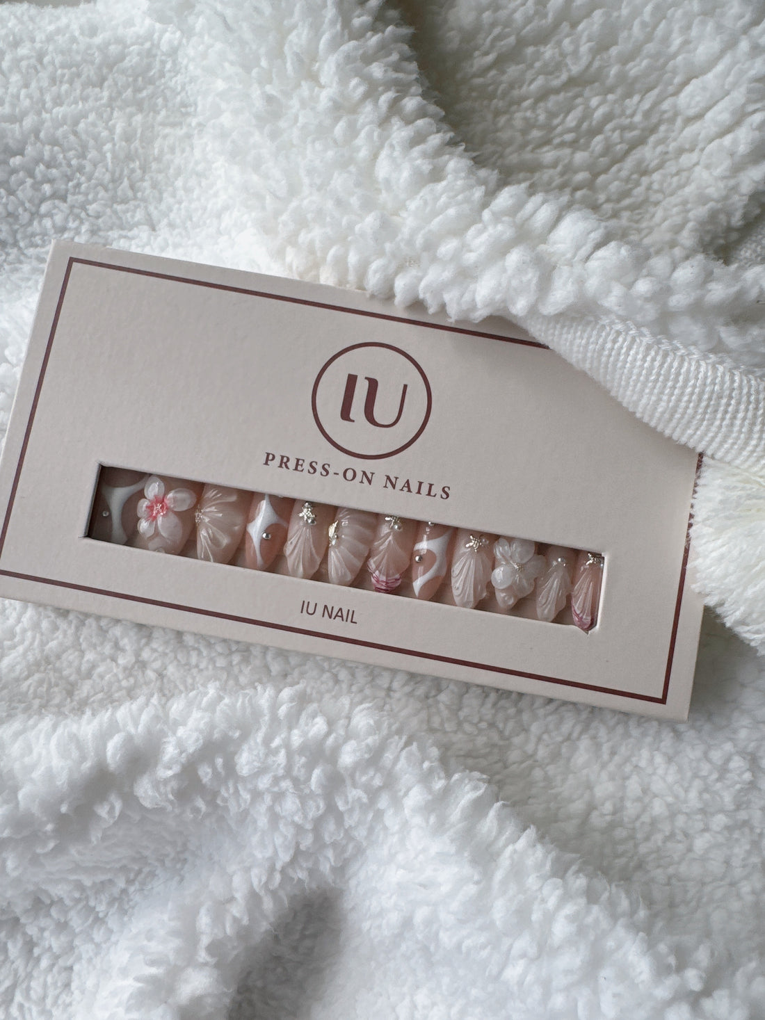 Box of pink and white press-on nails with floral and jeweled designs on white fabric