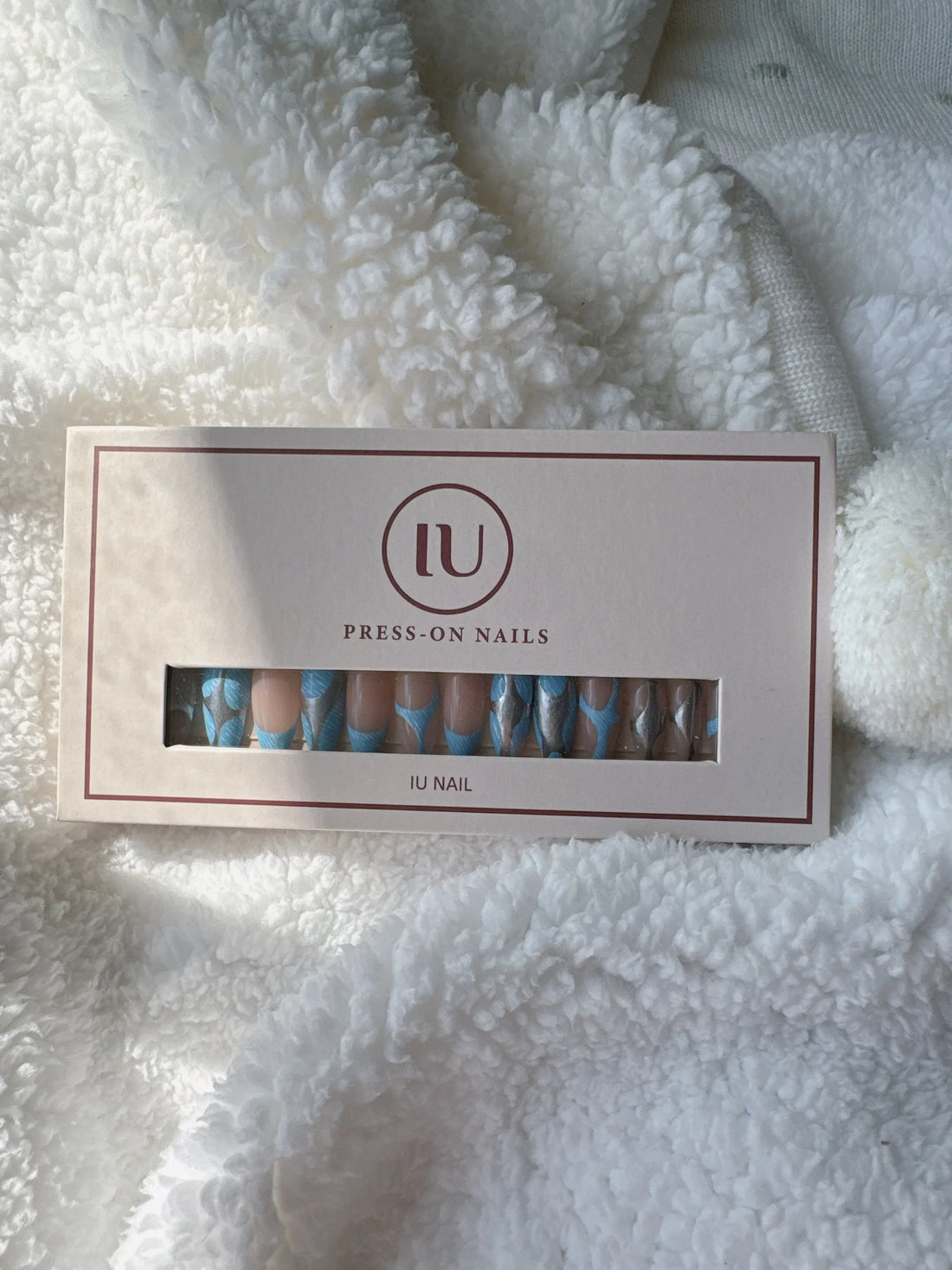 Blue and nude press-on nails set in box on white fluffy fabric background