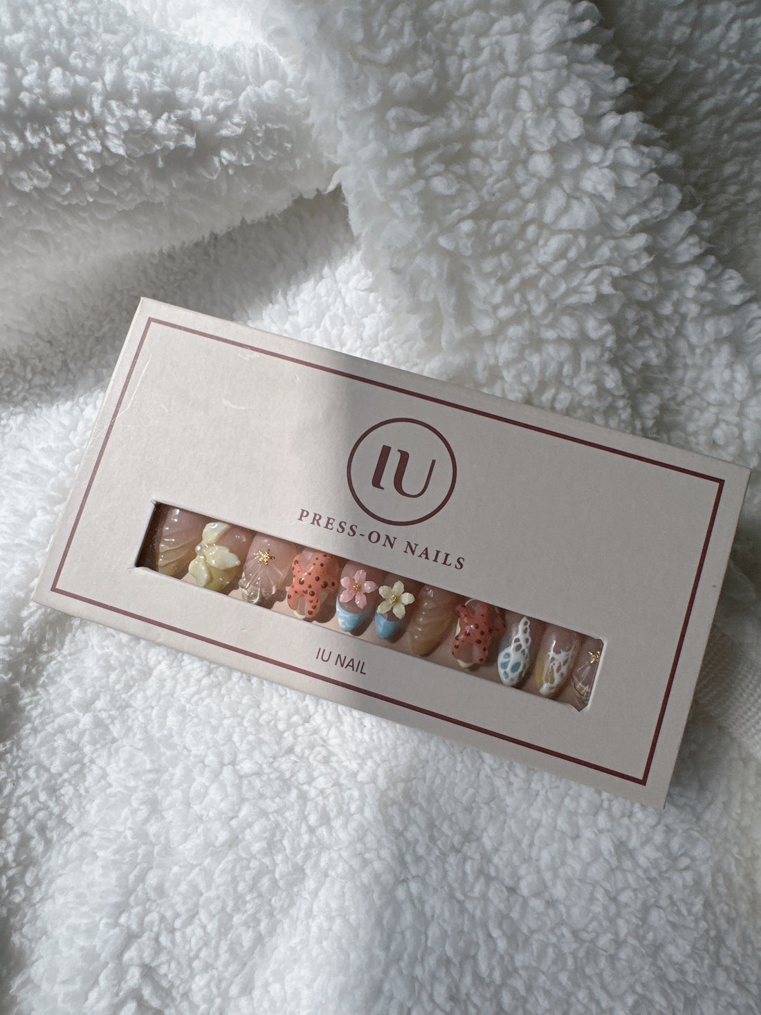 Box of colorful floral press-on nails with 3D designs on white textured fabric