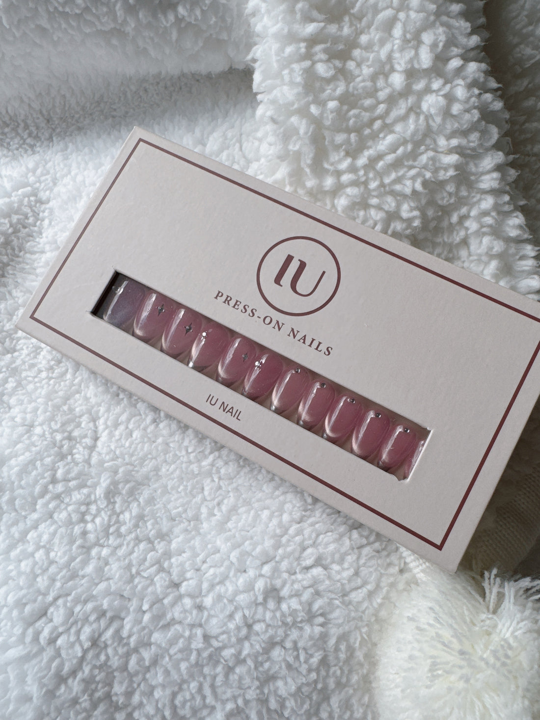 Box of pink press-on nails with small star accents on white textured fabric