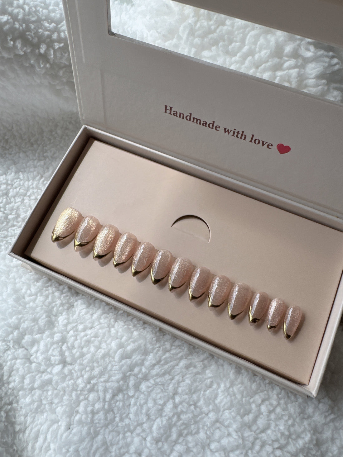 Box of nude and gold press-on nails on white textured fabric