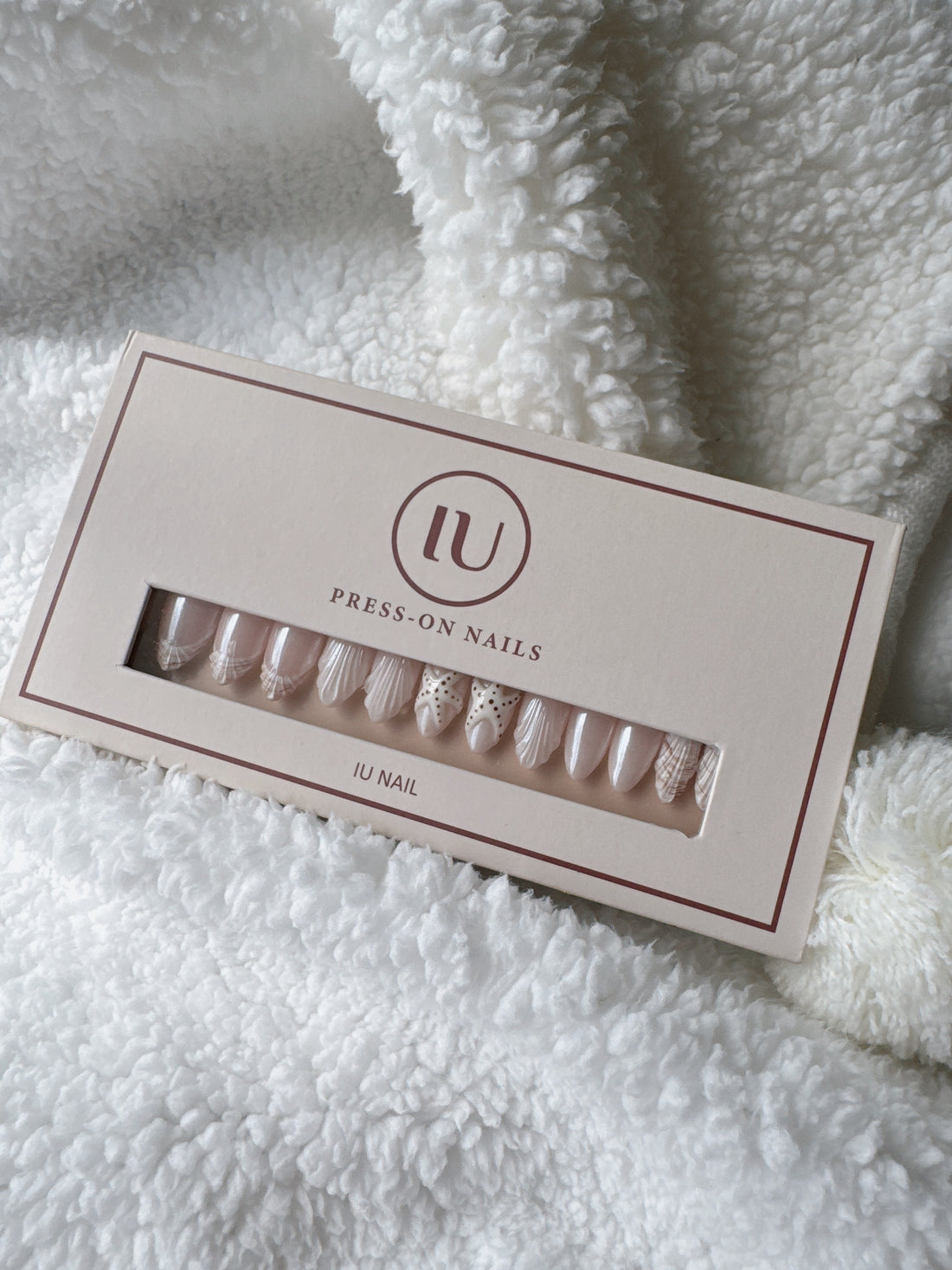 Box of nude and white press-on nails with delicate designs on soft white blanket