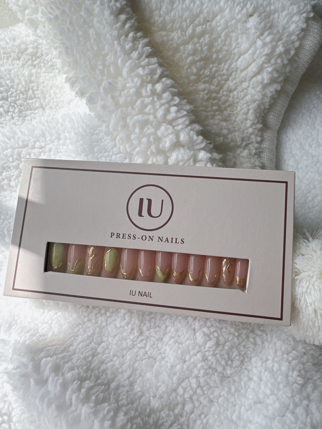 Box of nude and gold press-on nails on soft white textured fabric