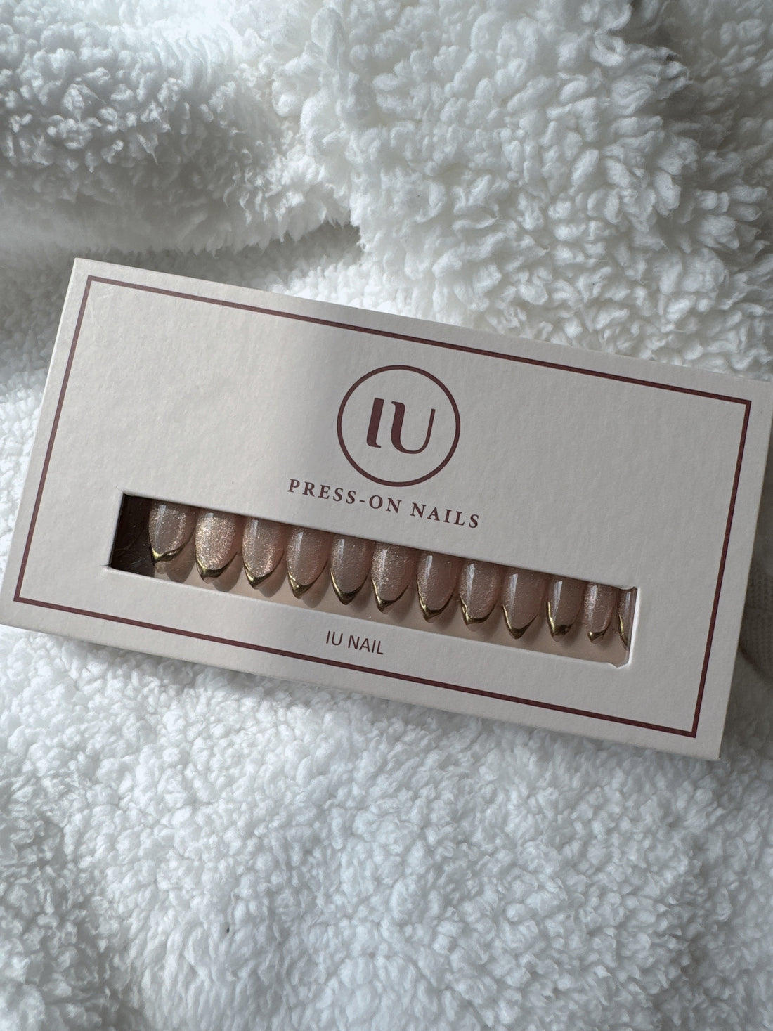 Box of nude and gold press-on nails on white textured fabric