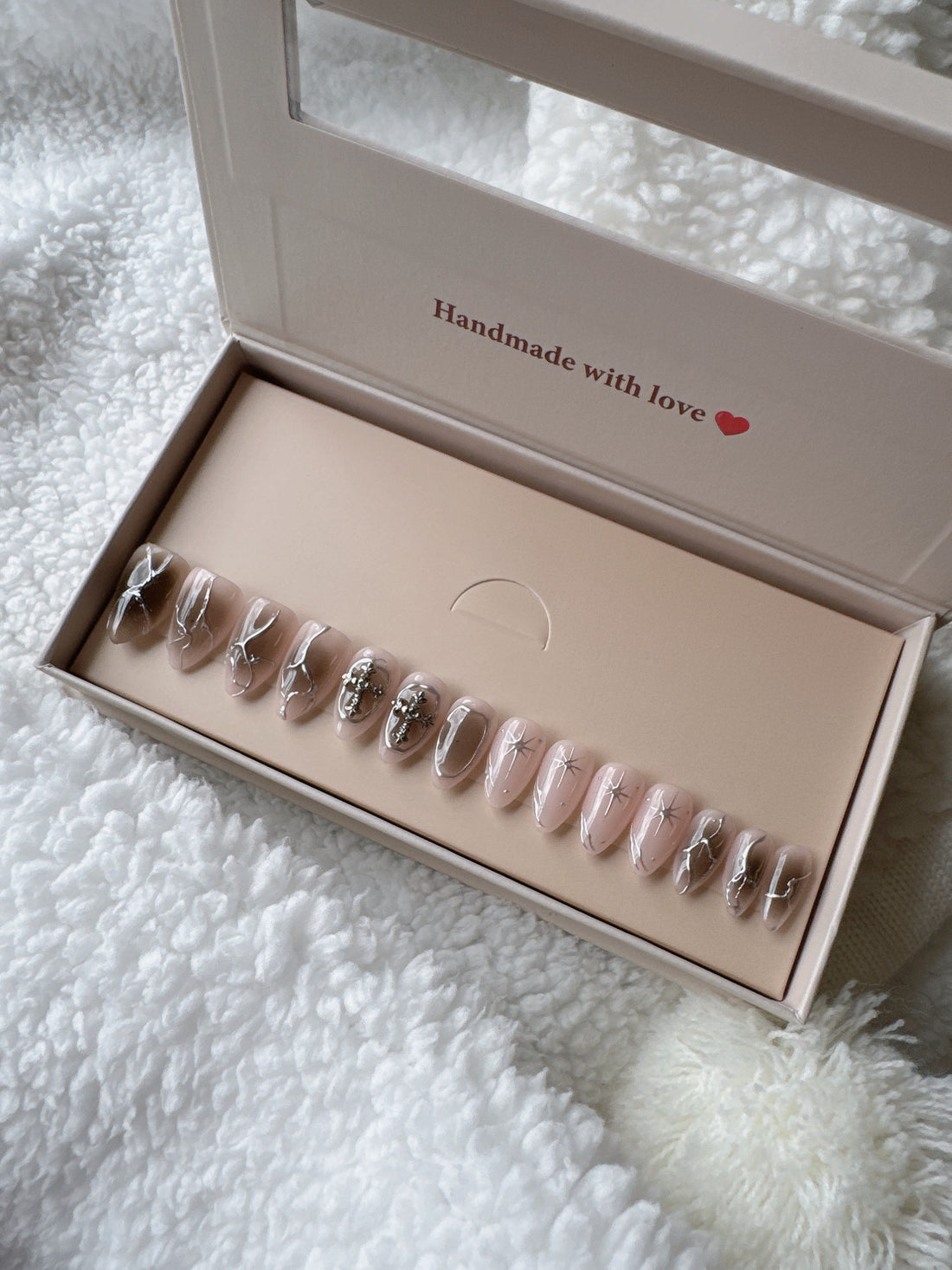 Box of nude and silver press-on nails with star and jewel accents on a white textured blanket