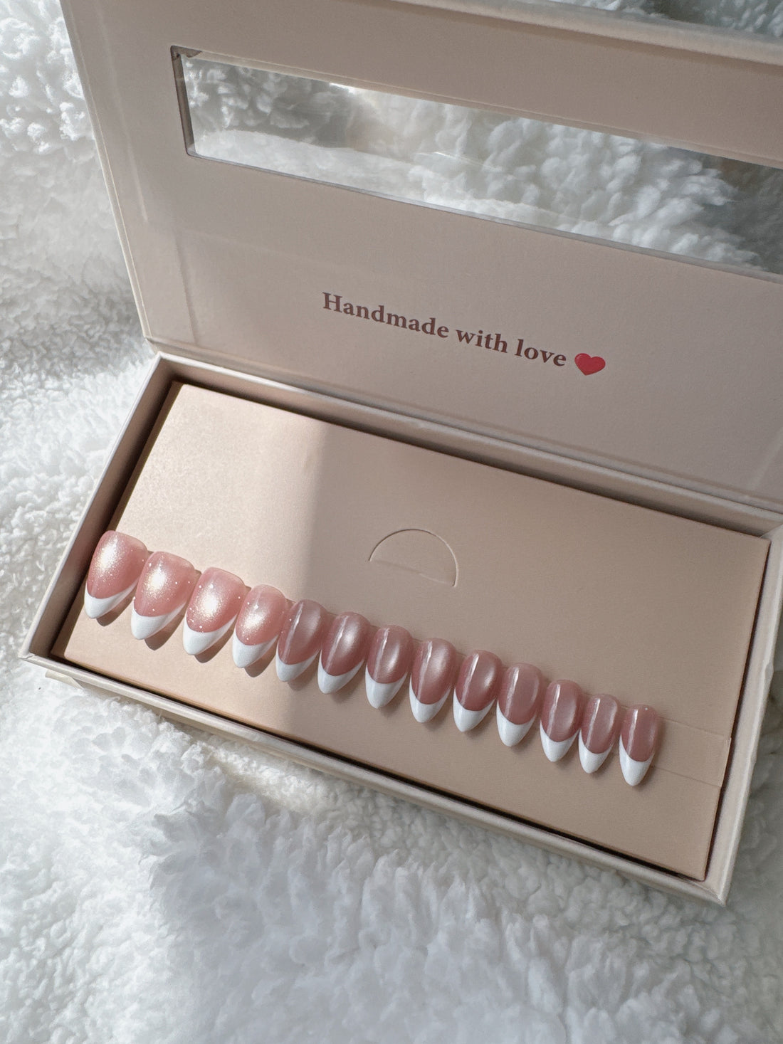 Pink and white French tip press-on nails set in box on soft white fabric background