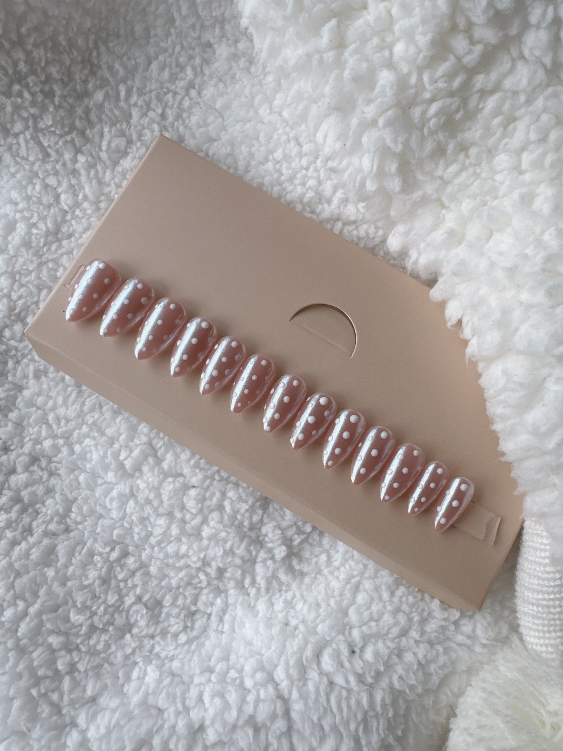 Almond-shaped press on nails with nude base and white polka dot design on display card
