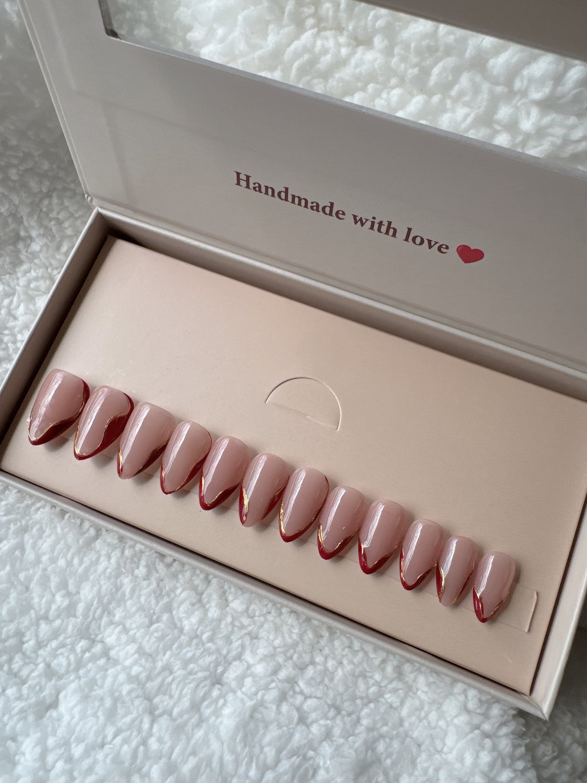 Coffin-shaped press-on nails in nude pink with red tips arranged in a gift box