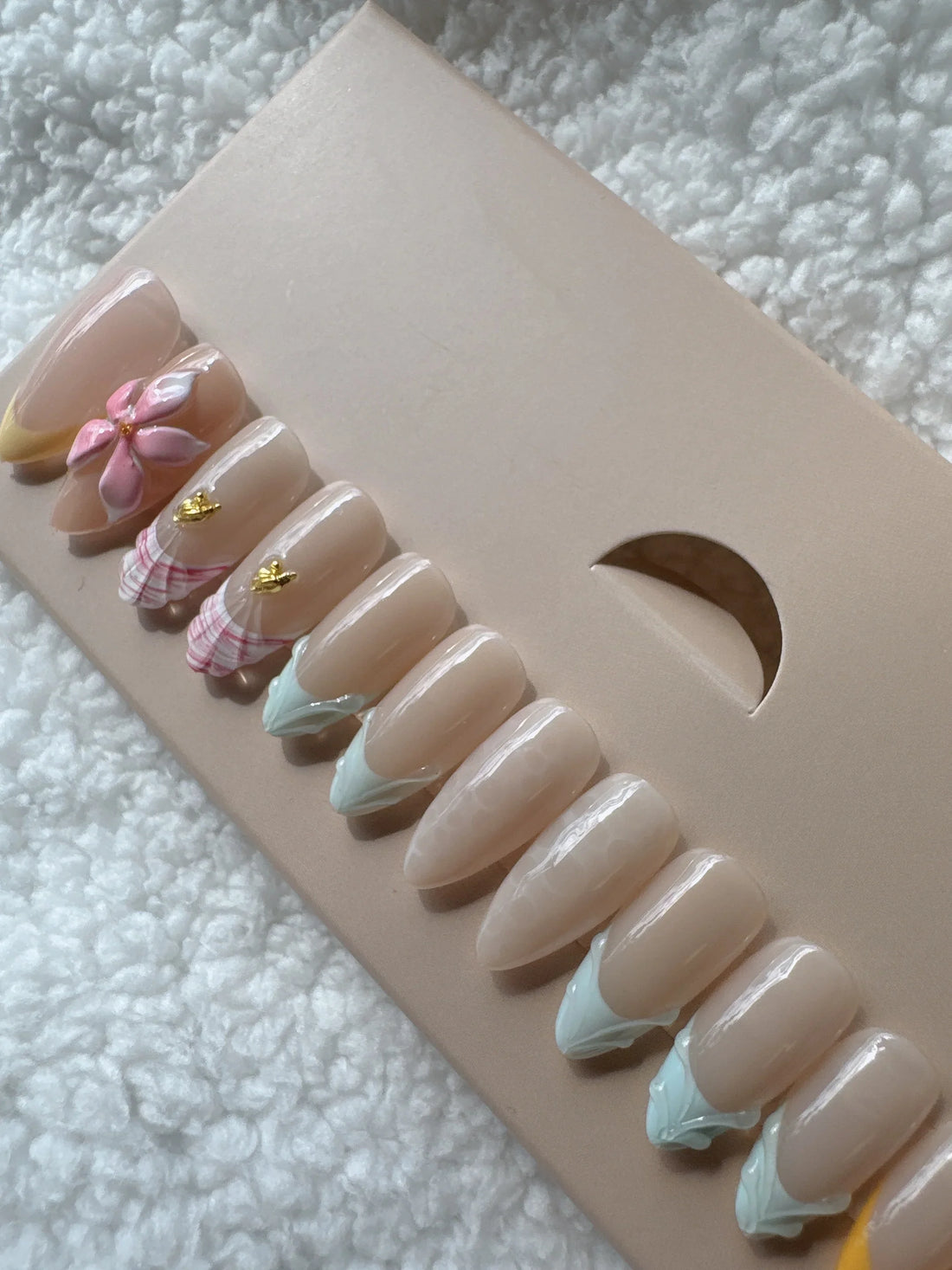 Box of press-on nails with floral and pastel designs on white textured fabric