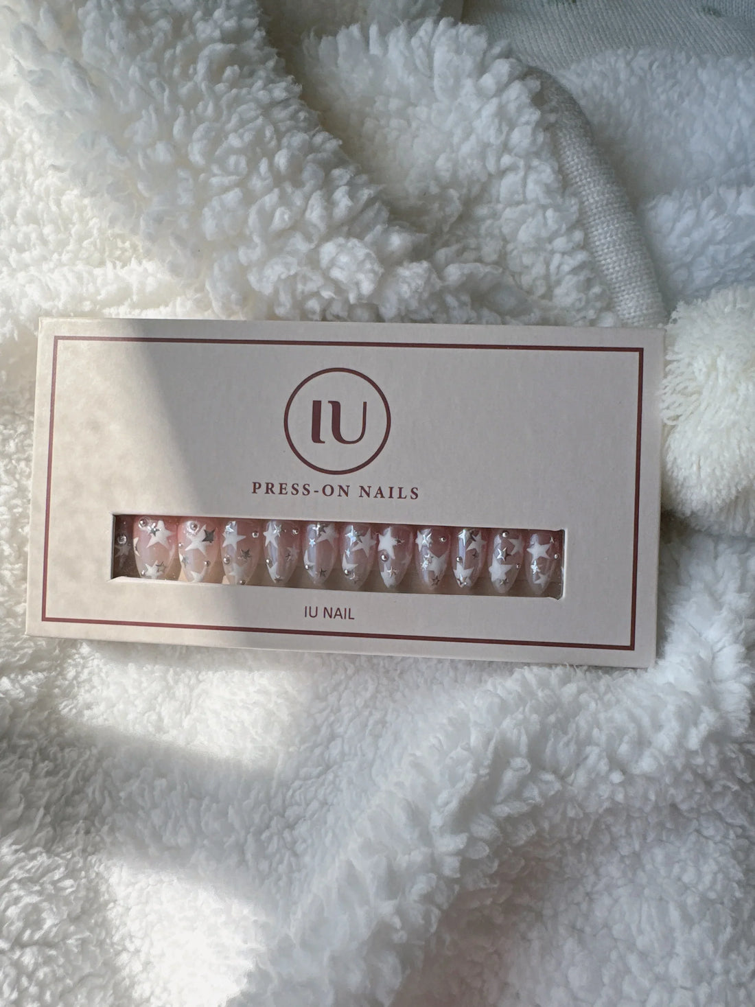 Box of pink press-on nails with white star and rhinestone designs on a soft white blanket
