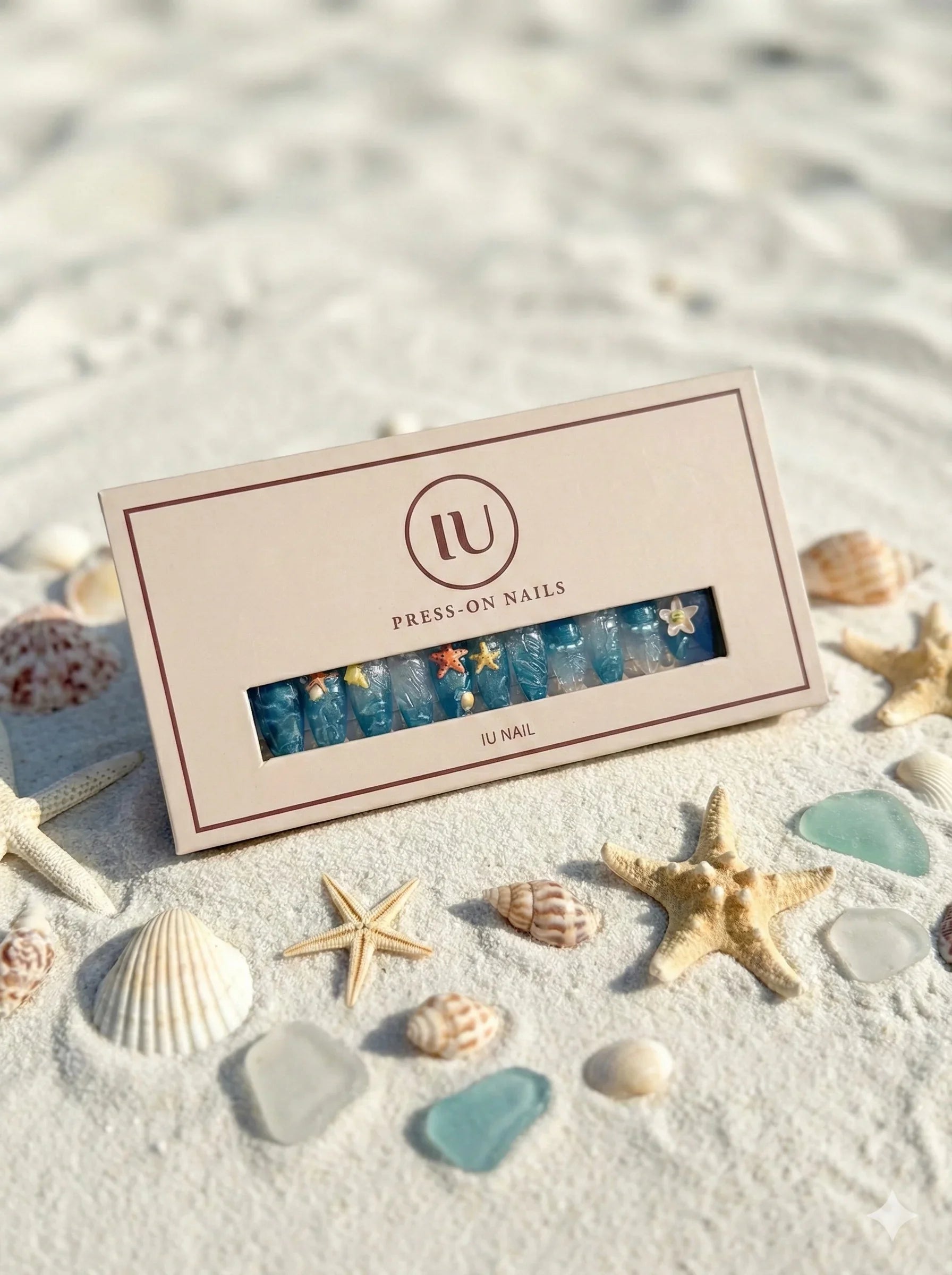 Beach-themed press-on nails in box with seashells and starfish on sandslider_item_qWiUeG