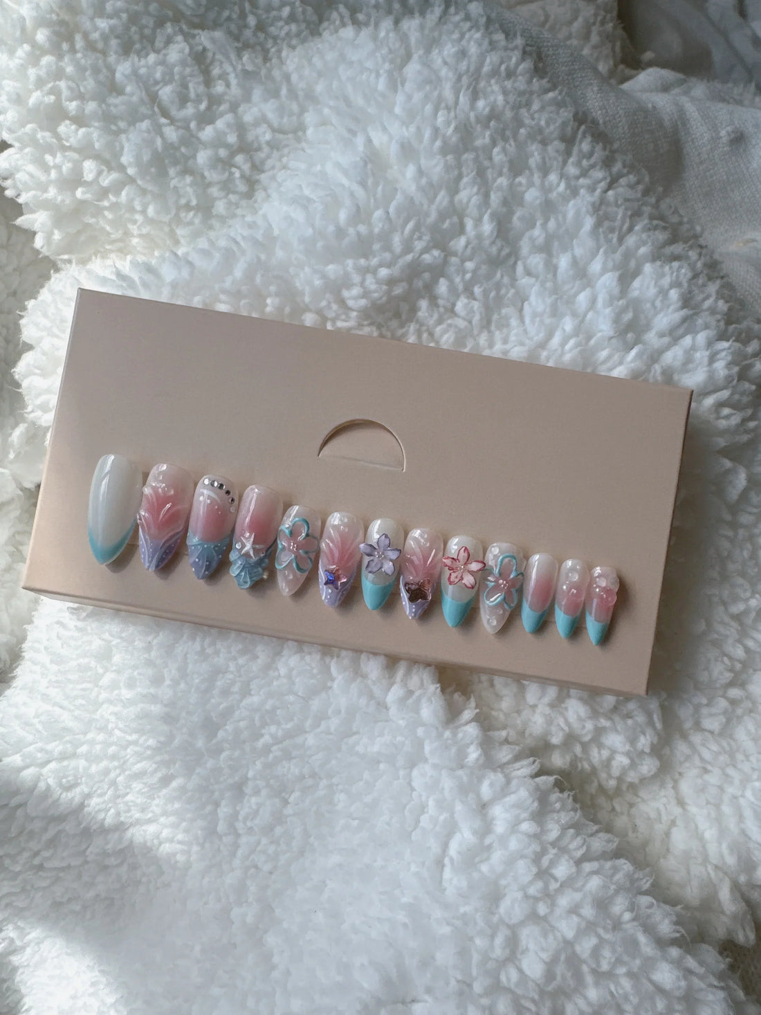 Pastel pink and blue press-on nails with floral designs displayed on a beige box