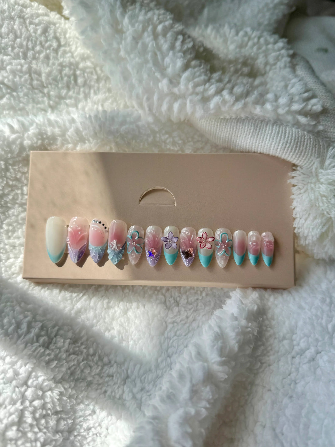 Pastel pink and blue press-on nails with floral designs displayed on a beige box